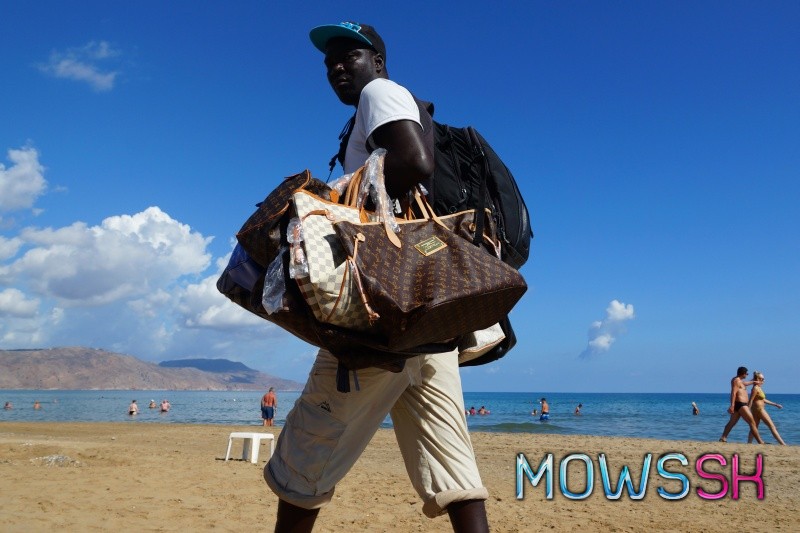 Imigrant na pláži predáva kabelky